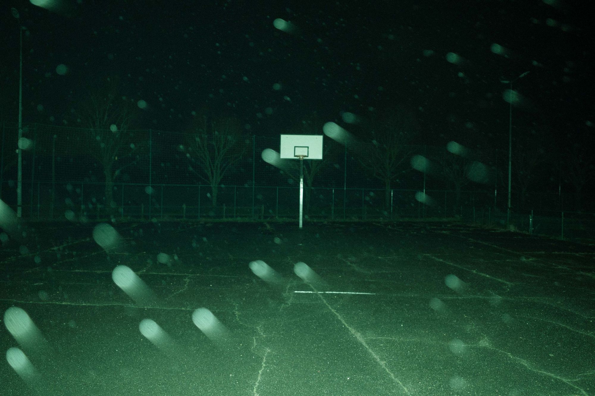 An empty outdoor basketball court at night with fog under the lights