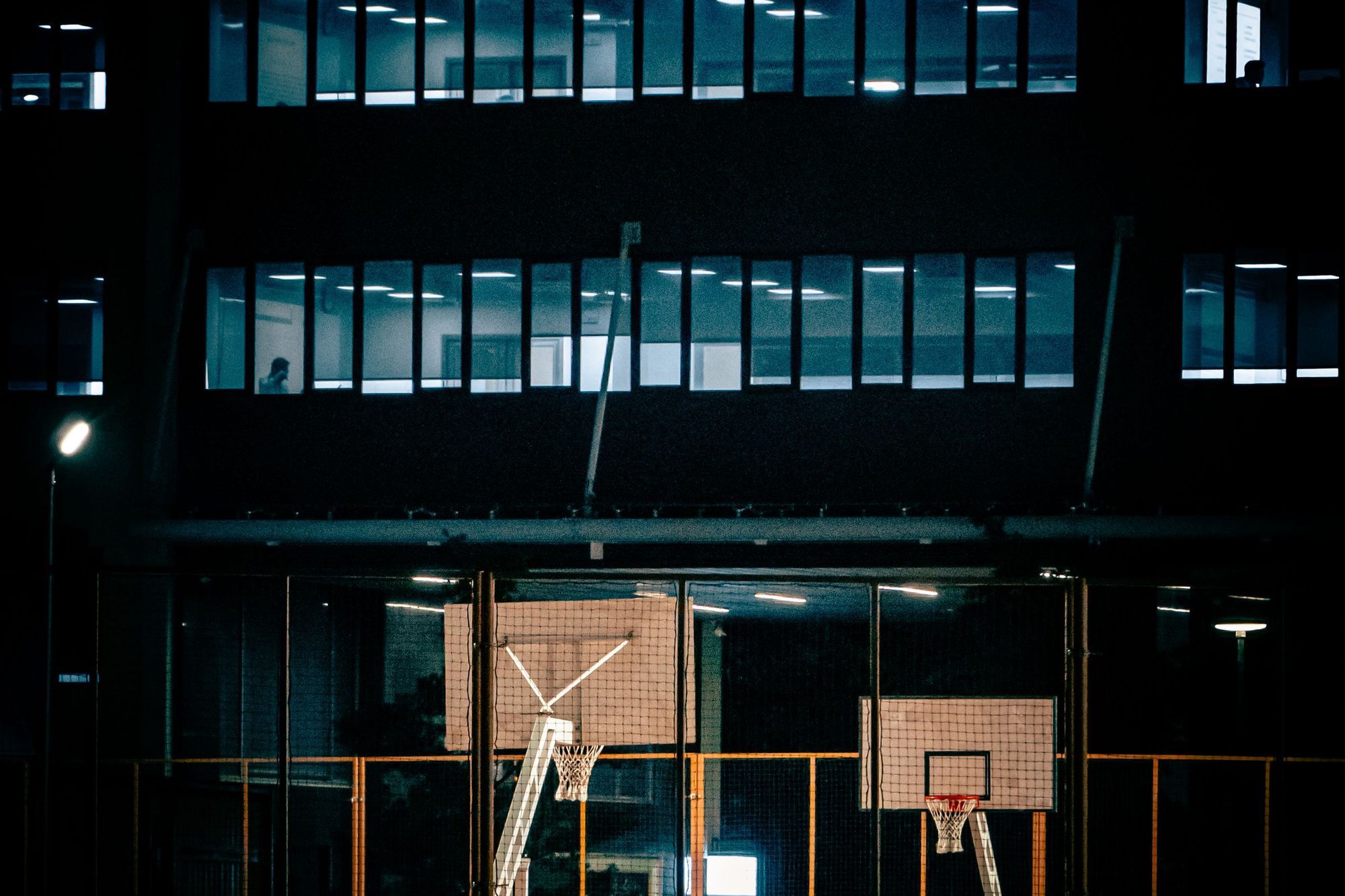 A quiet urban basketball court at night beneath lit apartment windows